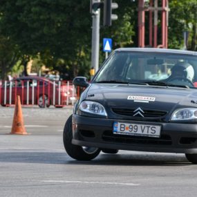 Black Citroen car takes a sharp turn during a street race in an urban setting.